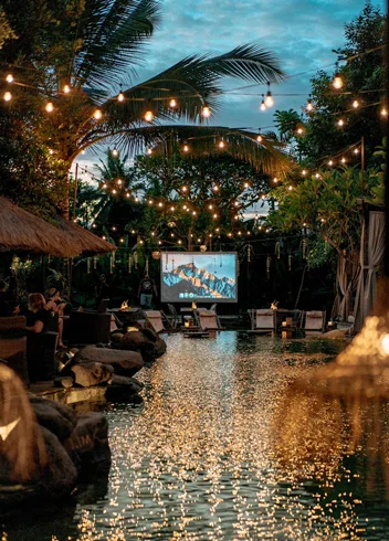 An outdoor cinema under festoon lights over water