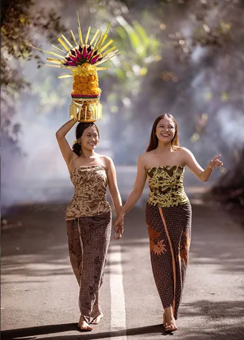 Two women in traditional dress carrying an offering